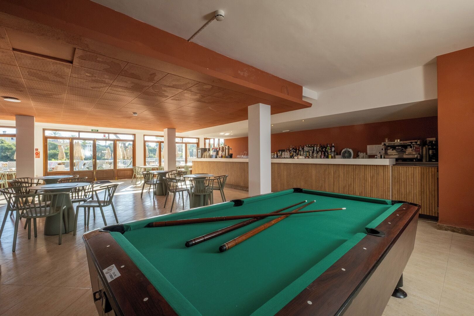 A pool table with cues, a bar area, and outdoor seating with a view.
