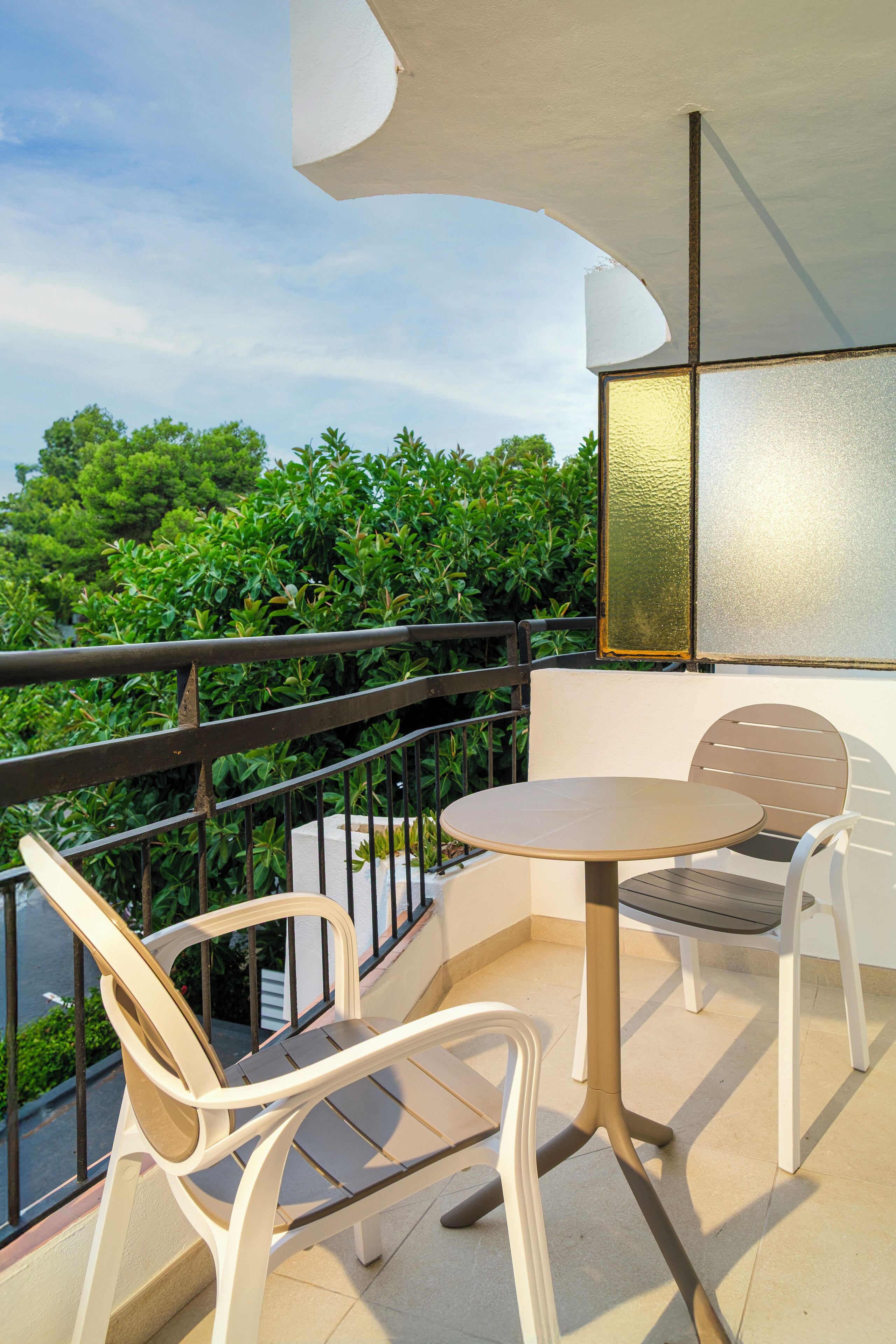 Ein Balkon mit rundem Tisch, zwei Stühlen, Geländer und Blick ins Grüne.