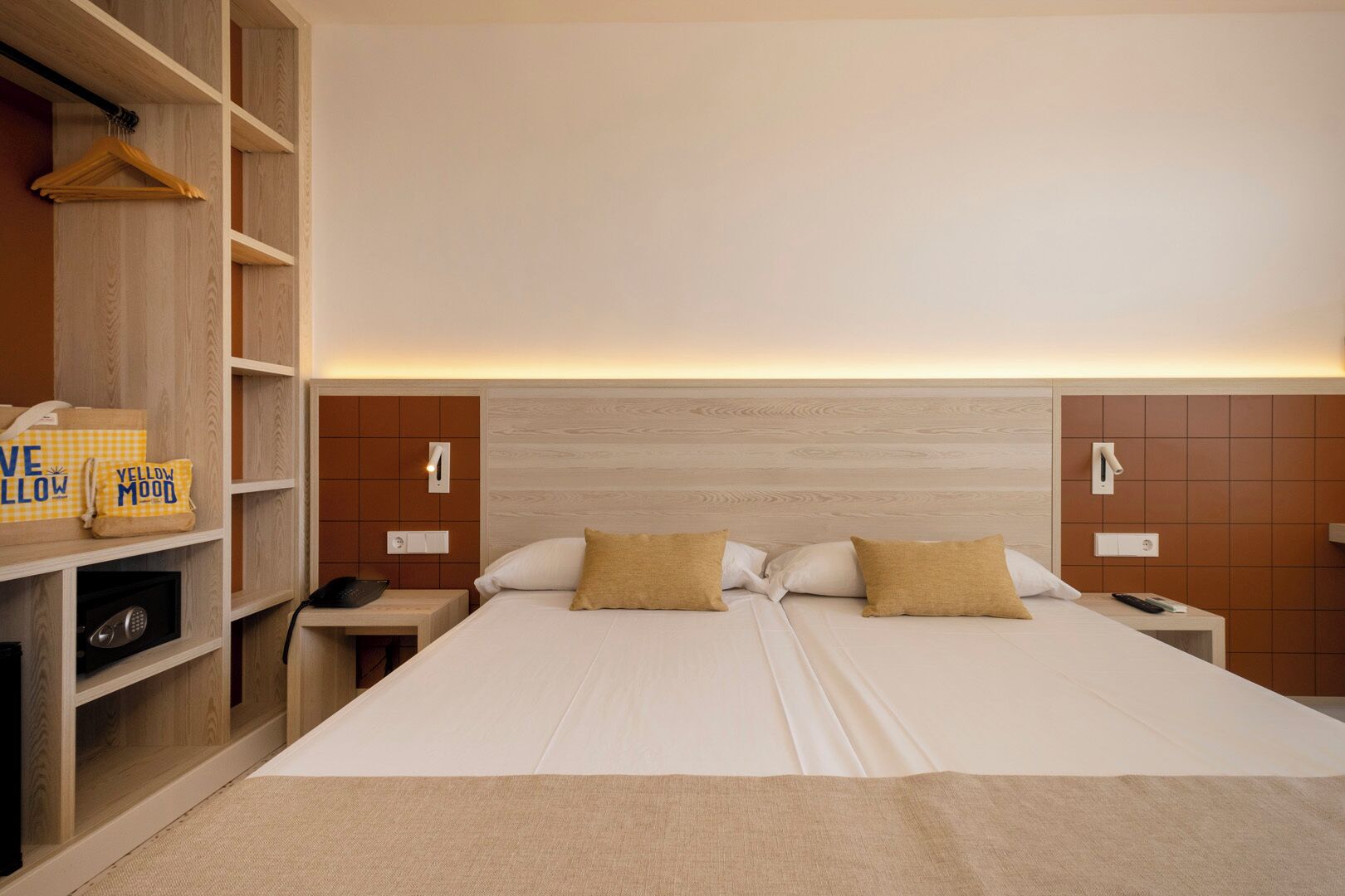 A hotel room with a bed, a nightstand, a shelf with hangers, and a small table with a lamp.
