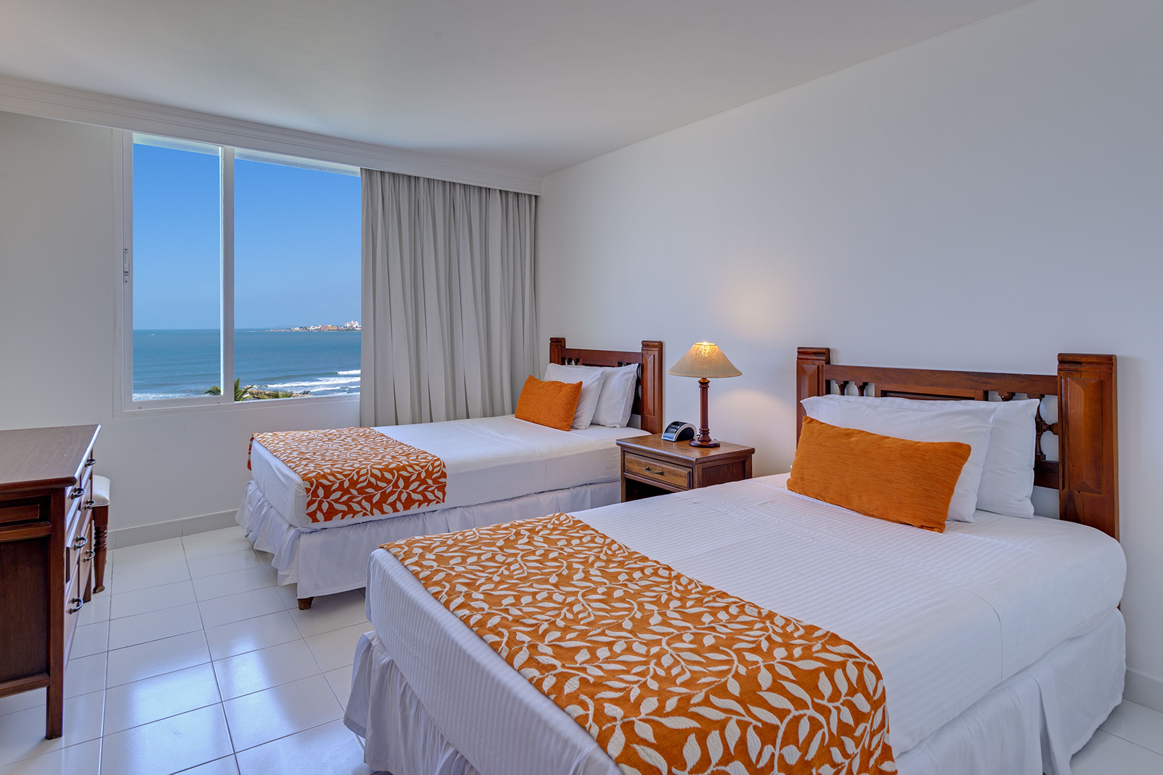 Habitación de hotel con dos camas, un escritorio y vista al océano.