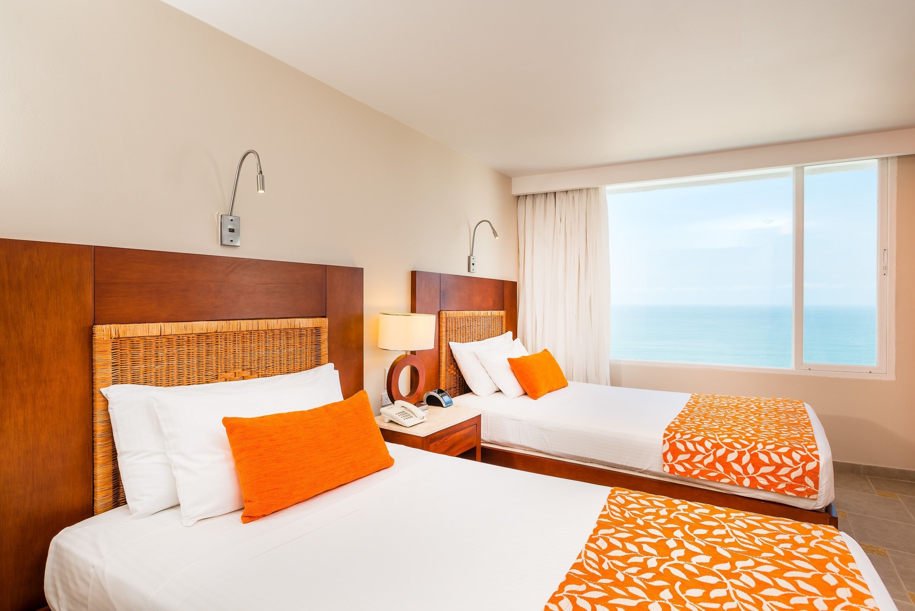 Une chambre d’hôtel avec deux lits, une table de chevet avec une lampe, un téléphone et une vue sur la mer.