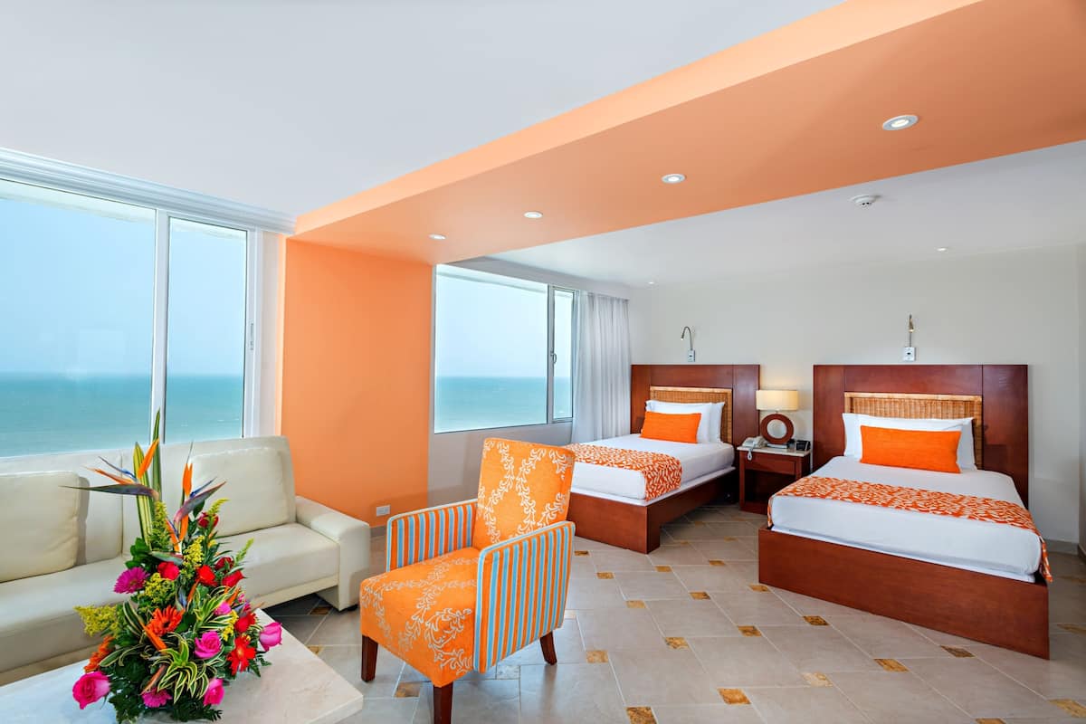 A hotel room with two beds, a sofa, a chair, and a view of the ocean.