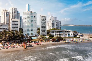 Un hotel frente a la playa con varios edificios de gran altura, una zona de piscina y sombrillas.