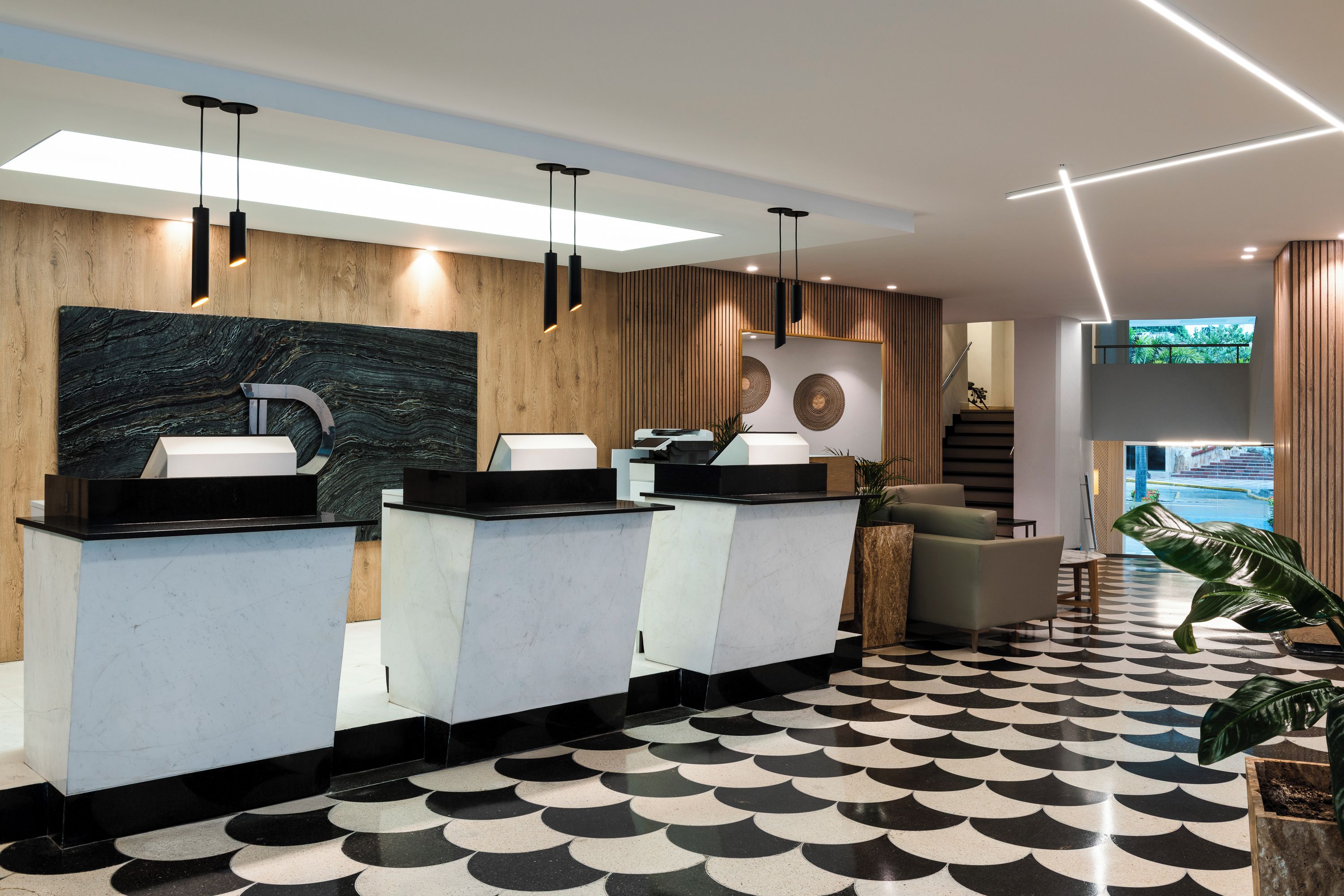 Un espace d’accueil au design moderne, comprenant un comptoir d’enregistrement, un coin salon et un escalier menant à un niveau supérieur.