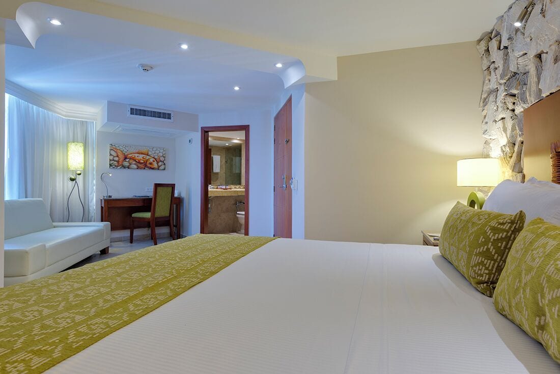 A hotel room with a large bed, a desk, a chair, and a bathroom visible through an open door.