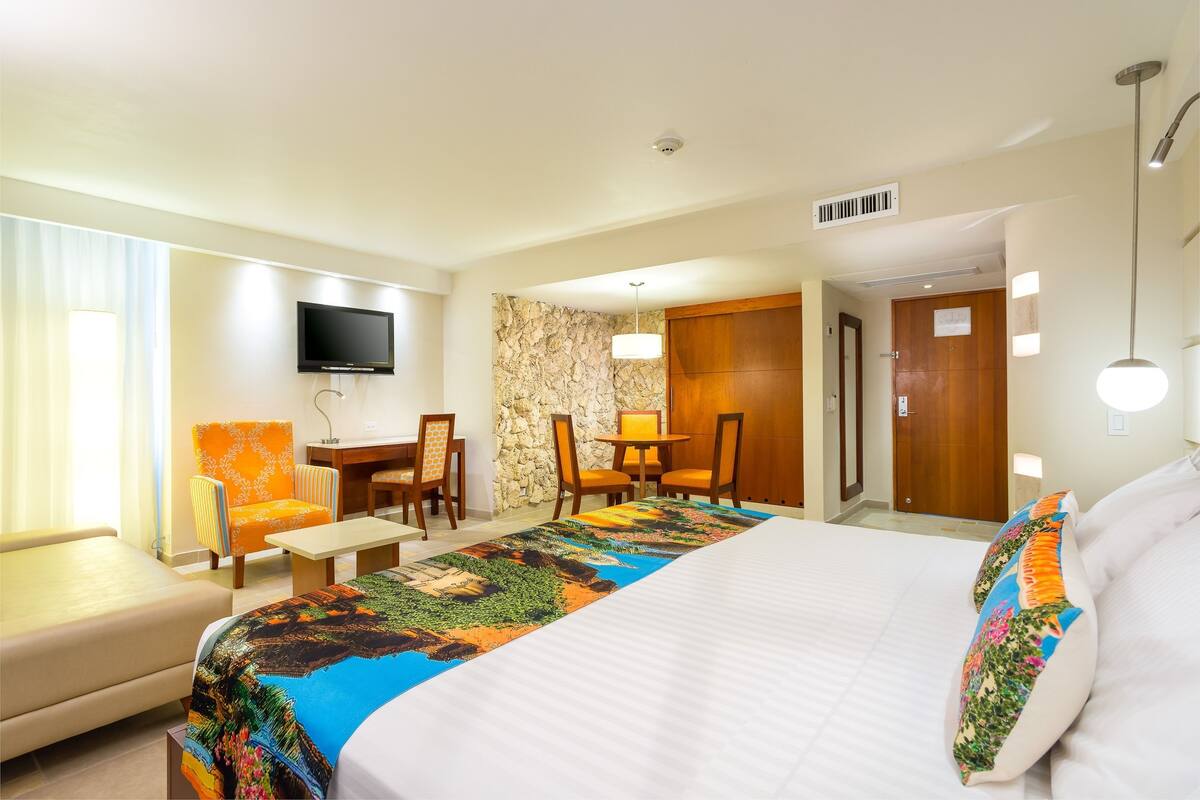 A hotel room with a large bed, a desk with a chair, a TV mounted on the wall, and a stone accent wall.
