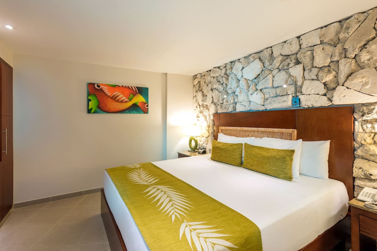 A hotel room with a bed, a stone wall, a painting, and a nightstand.
