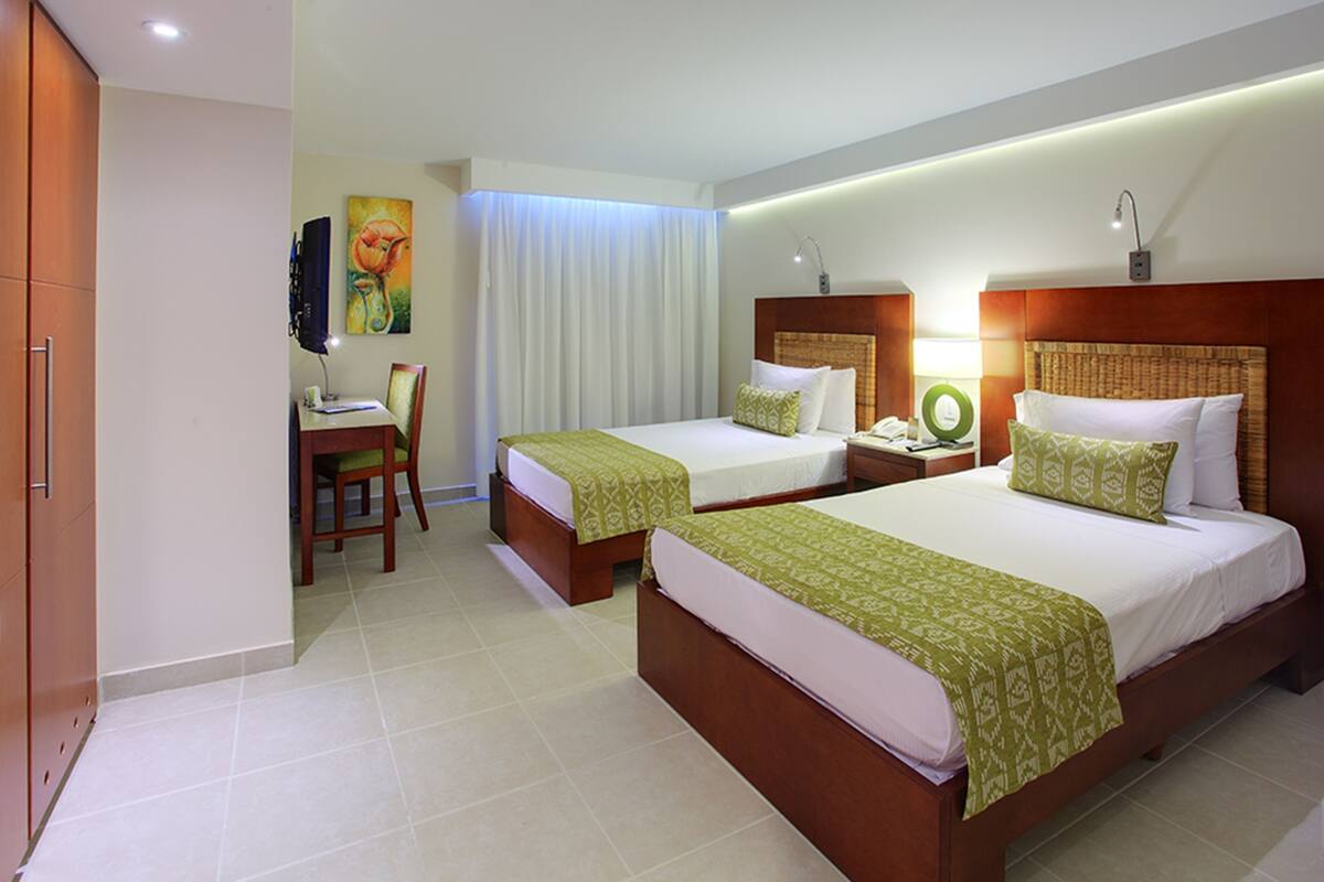 A hotel room with two beds, a desk, a chair, and a painting on the wall.