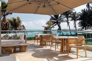 Una terraza con vista al océano, amueblada con sillones de mimbre y un sofá, y una sombrilla grande que proporciona sombra.