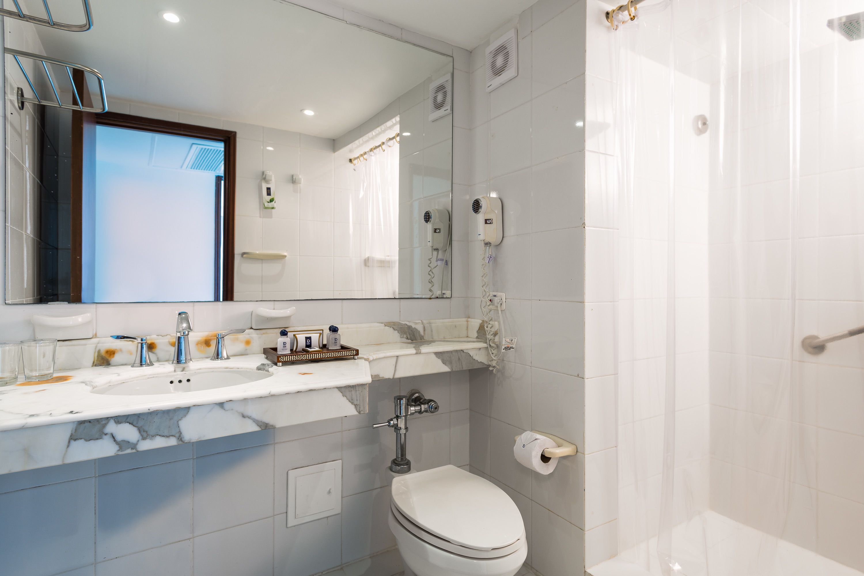 A modern bathroom with a marble sink, a toilet, a shower, and a large mirror.