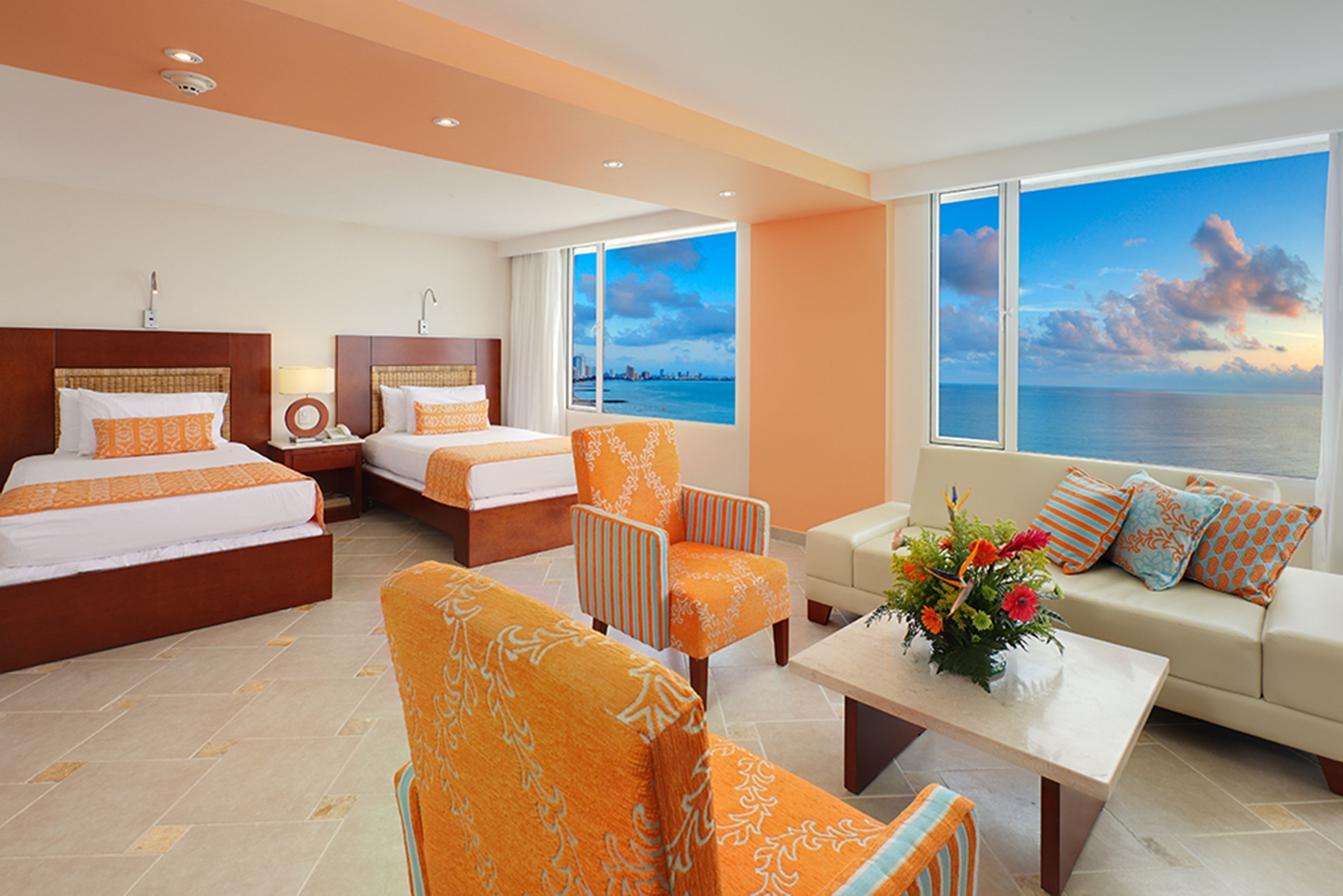 Habitación de hotel con dos camas, un sofá, una silla y vista al mar.