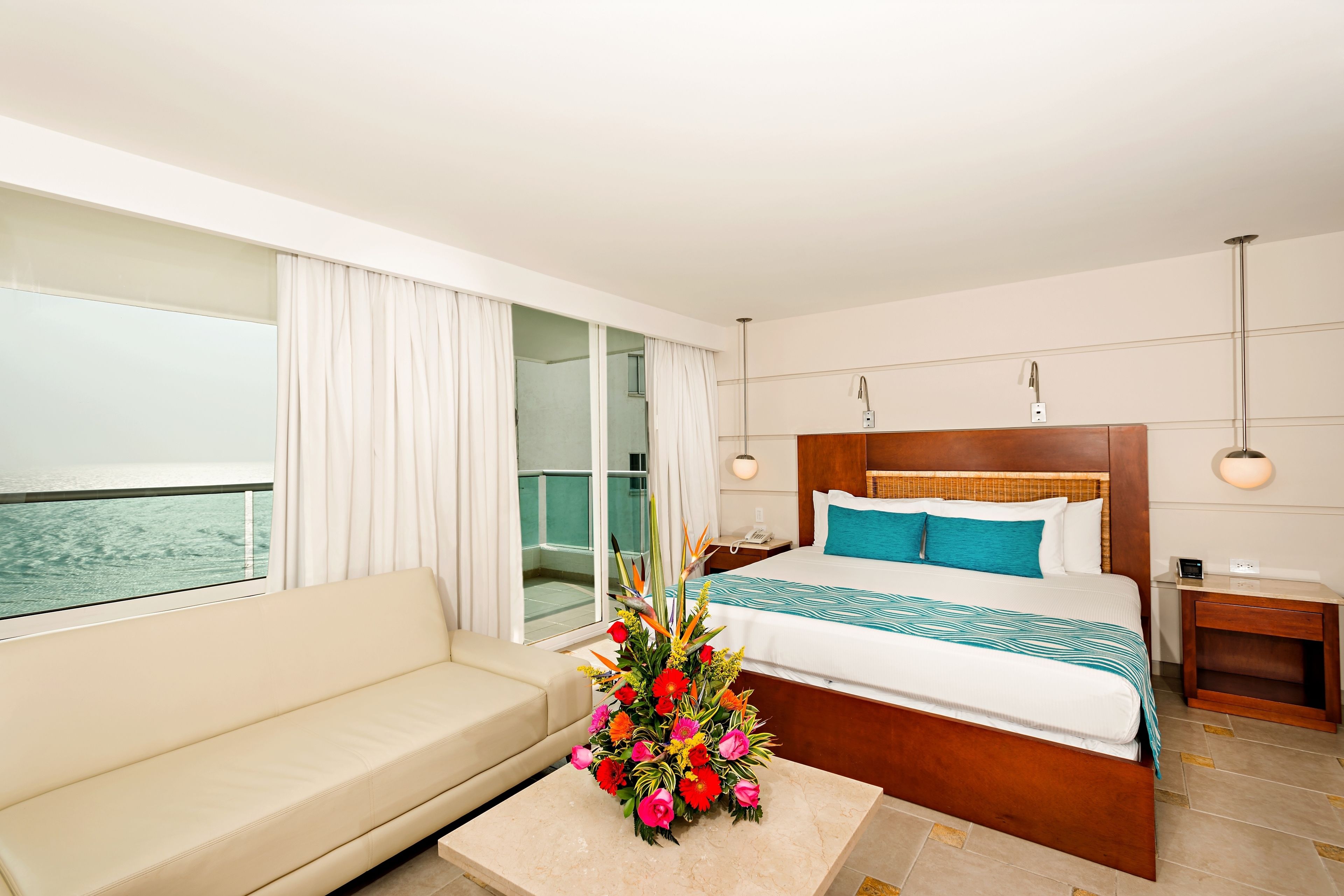 Una habitación de hotel con cama, sofá, mesita de noche y vista al mar.