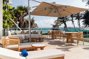 A sunlit outdoor seating area with a sofa, chairs, and a table, overlooking a body of water with palm trees. - Hotel Dann Cartagena (Cartagena)