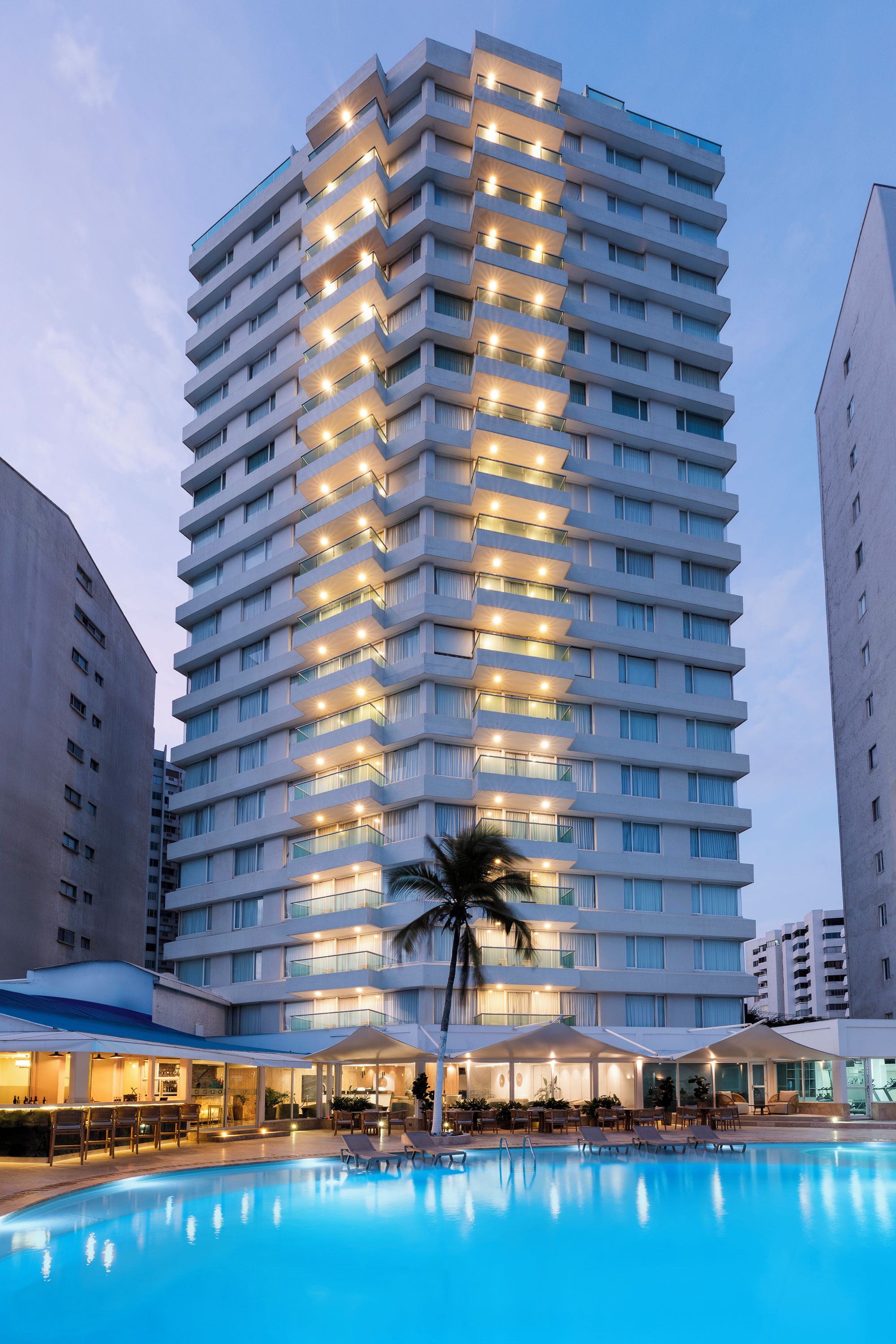 A high-rise hotel with multiple balconies, a swimming pool, and a bar area.