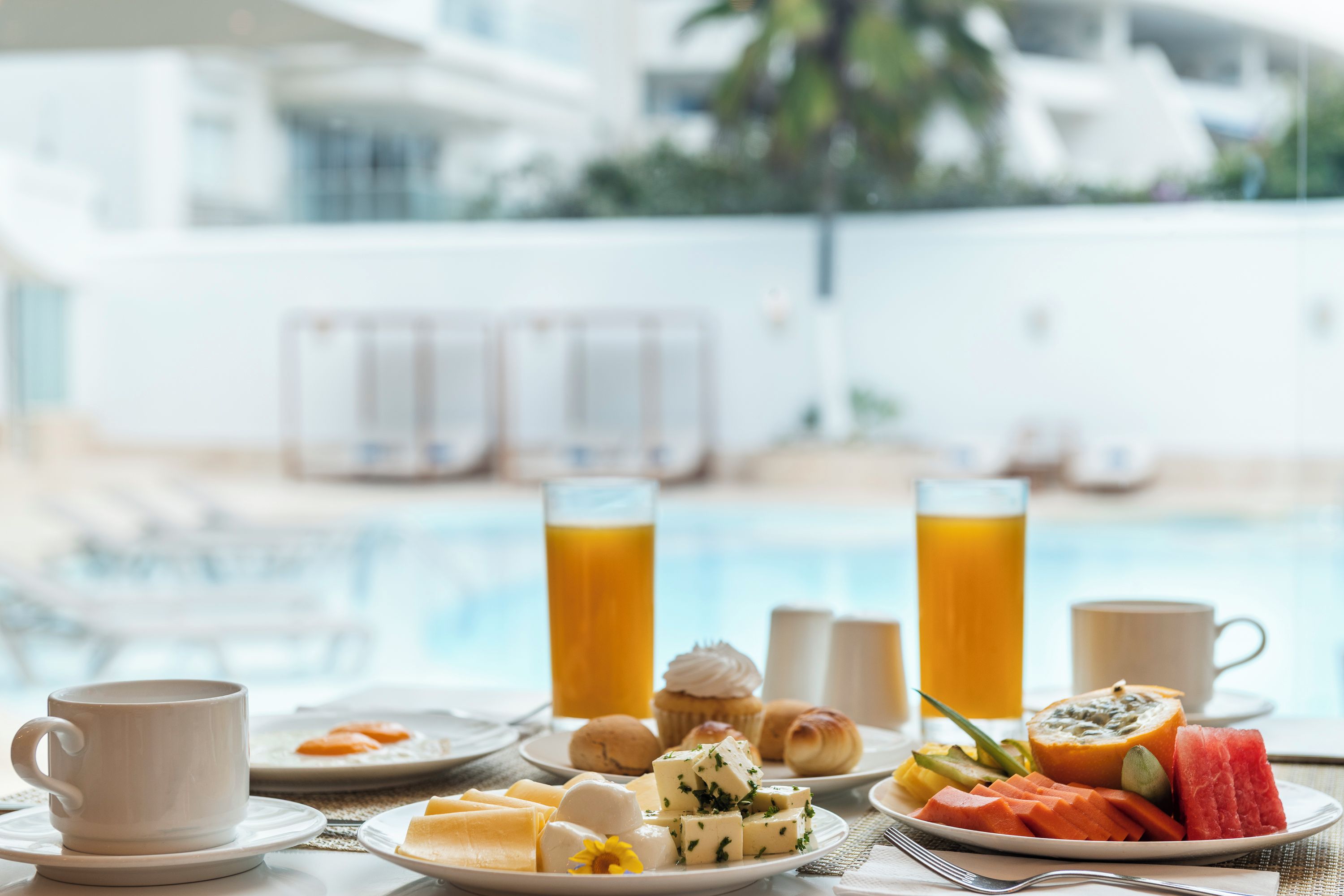 Une table dressée pour le petit-déjeuner avec vue sur la piscine, comprenant des assiettes de nourriture, une tasse et des verres de jus de fruits.
