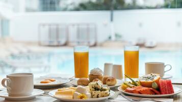 Une table dressée pour le petit-déjeuner avec vue sur la piscine, comprenant des assiettes de nourriture, une tasse et des verres de jus de fruits.