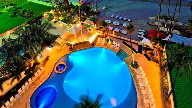 An aerial view of a resort with a large swimming pool, palm trees, and a beach. - Hotel Dann Cartagena (Cartagena)