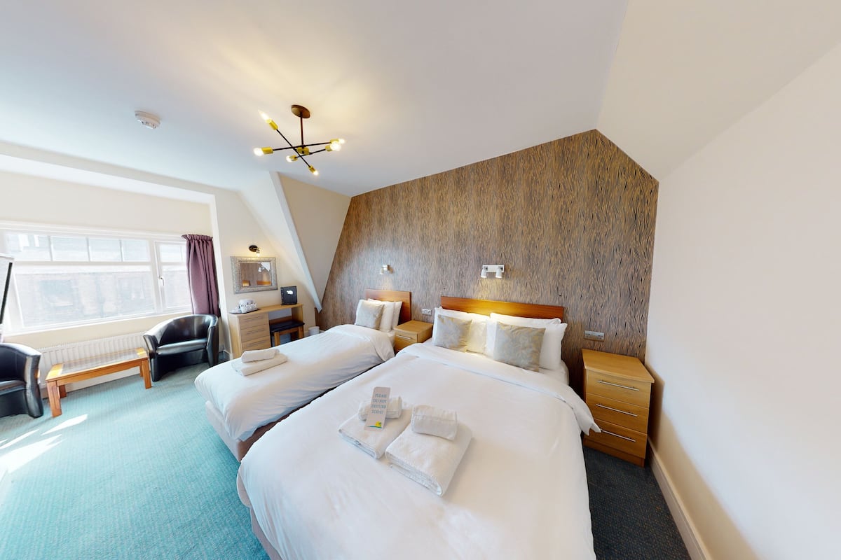 Een hotelkamer met twee bedden, een bureau, een stoel en een groot raam.