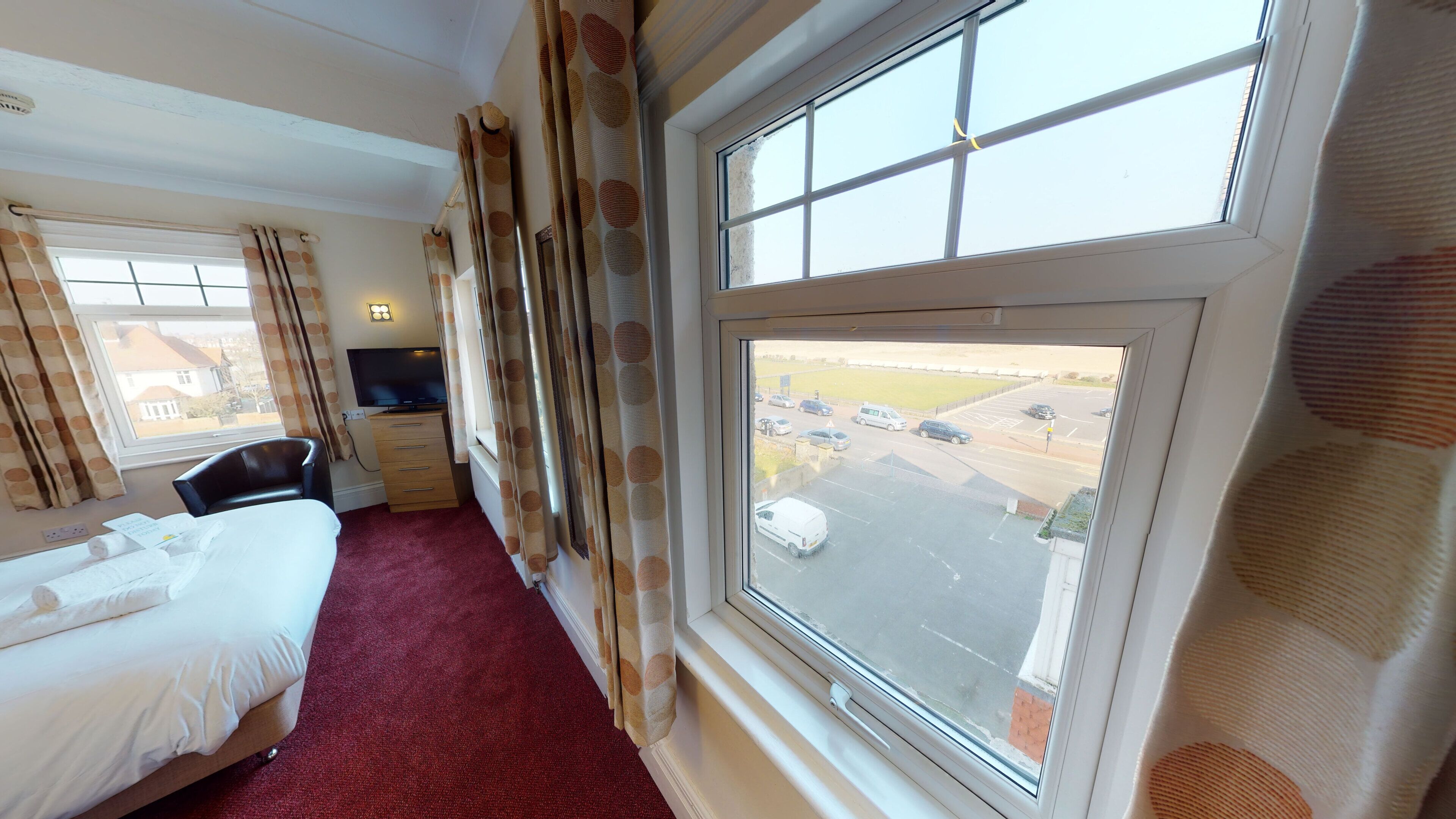 A hotel room with a bed, a desk, a TV, and a large window with a view of a parking lot.
