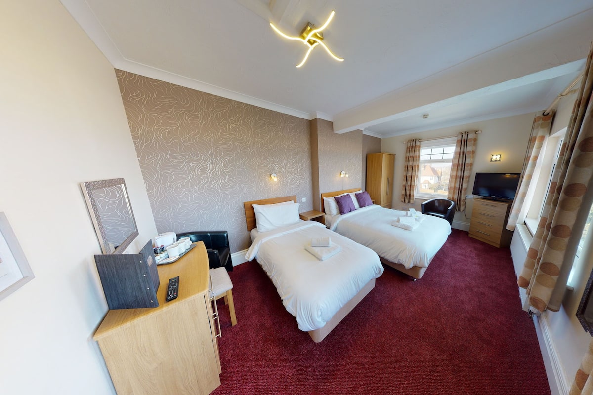 Een hotelkamer met twee bedden, een bureau met stoel, een televisie en een kledingkast.