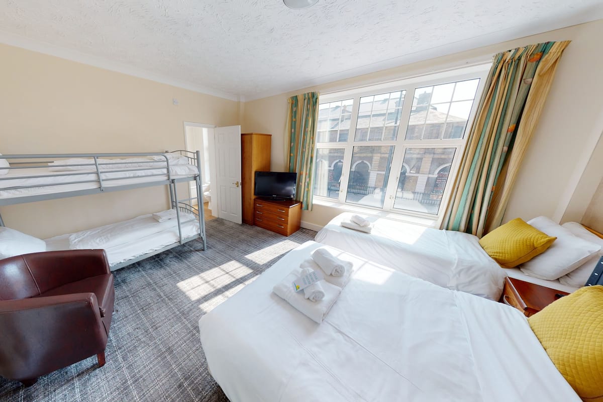 Een hotelkamer met stapelbedden, een eenpersoonsbed, een televisie, een bureau en een stoel.