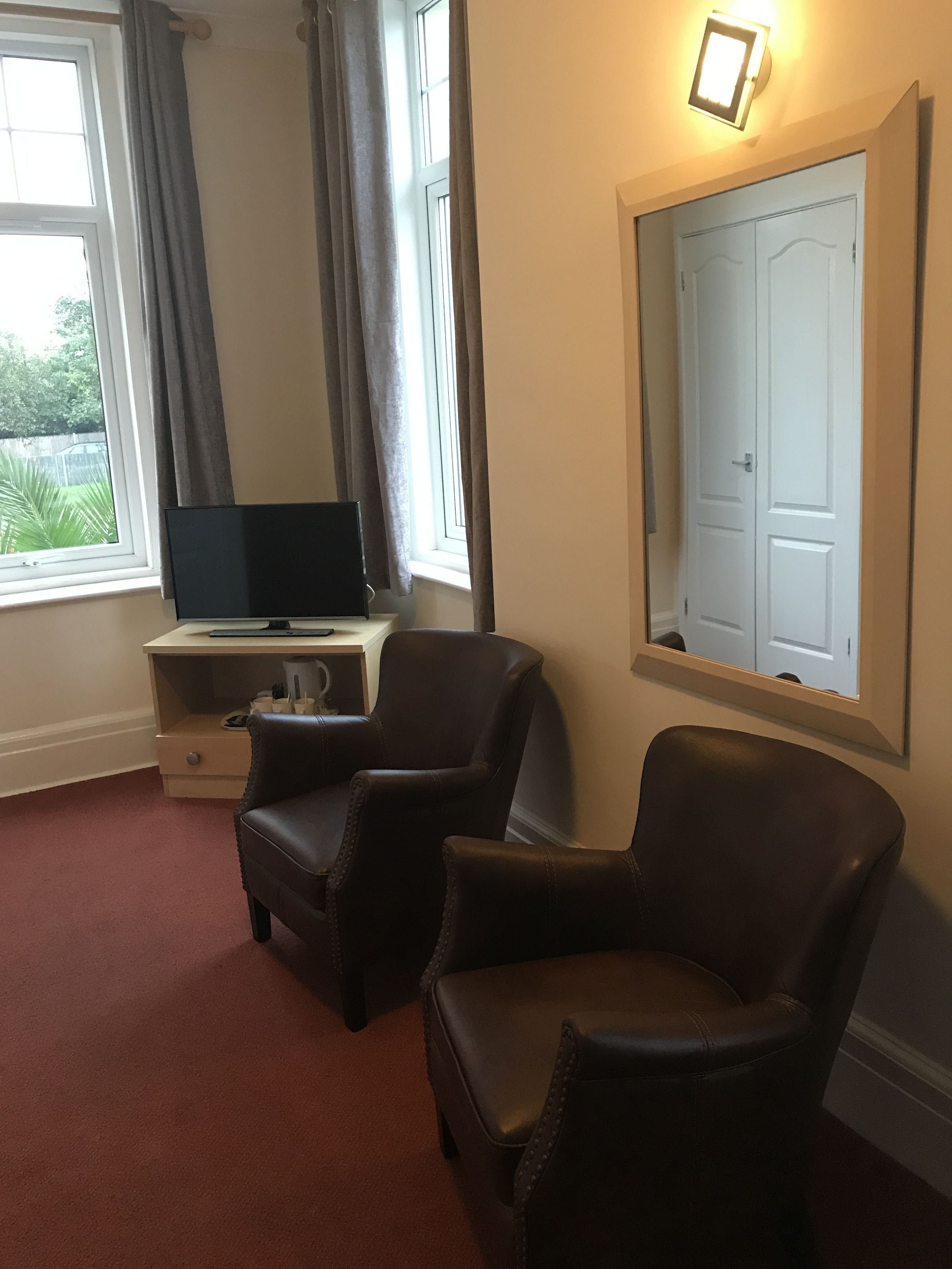 Una habitación con un escritorio, dos sillones de cuero, un televisor y un espejo grande en la pared.