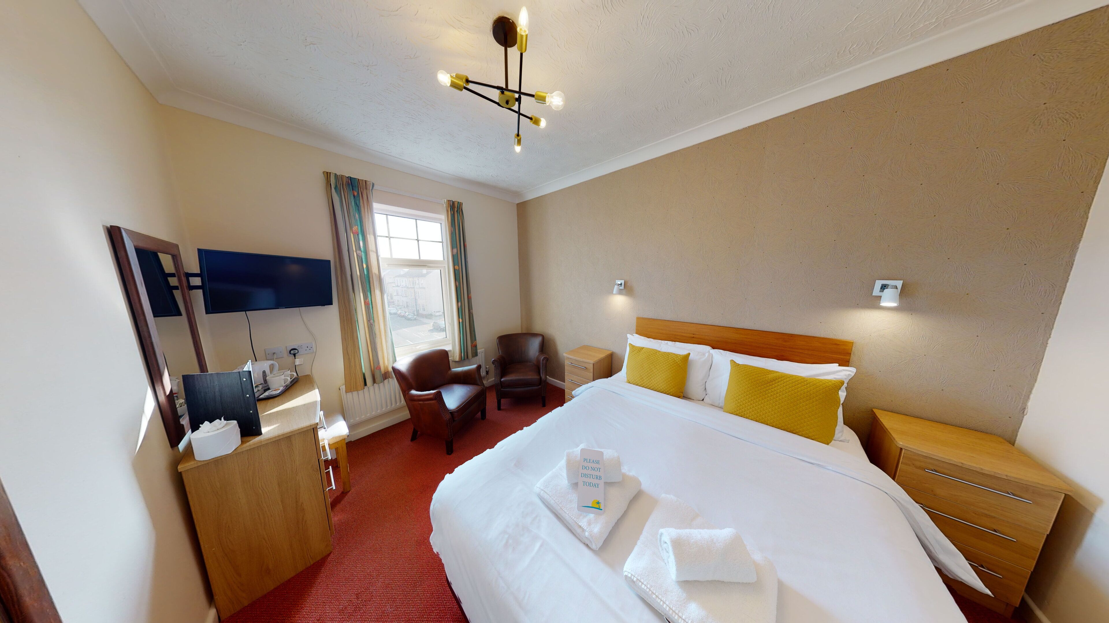 A hotel room with a bed, bedside table, chair, desk, TV, and a window with curtains.
