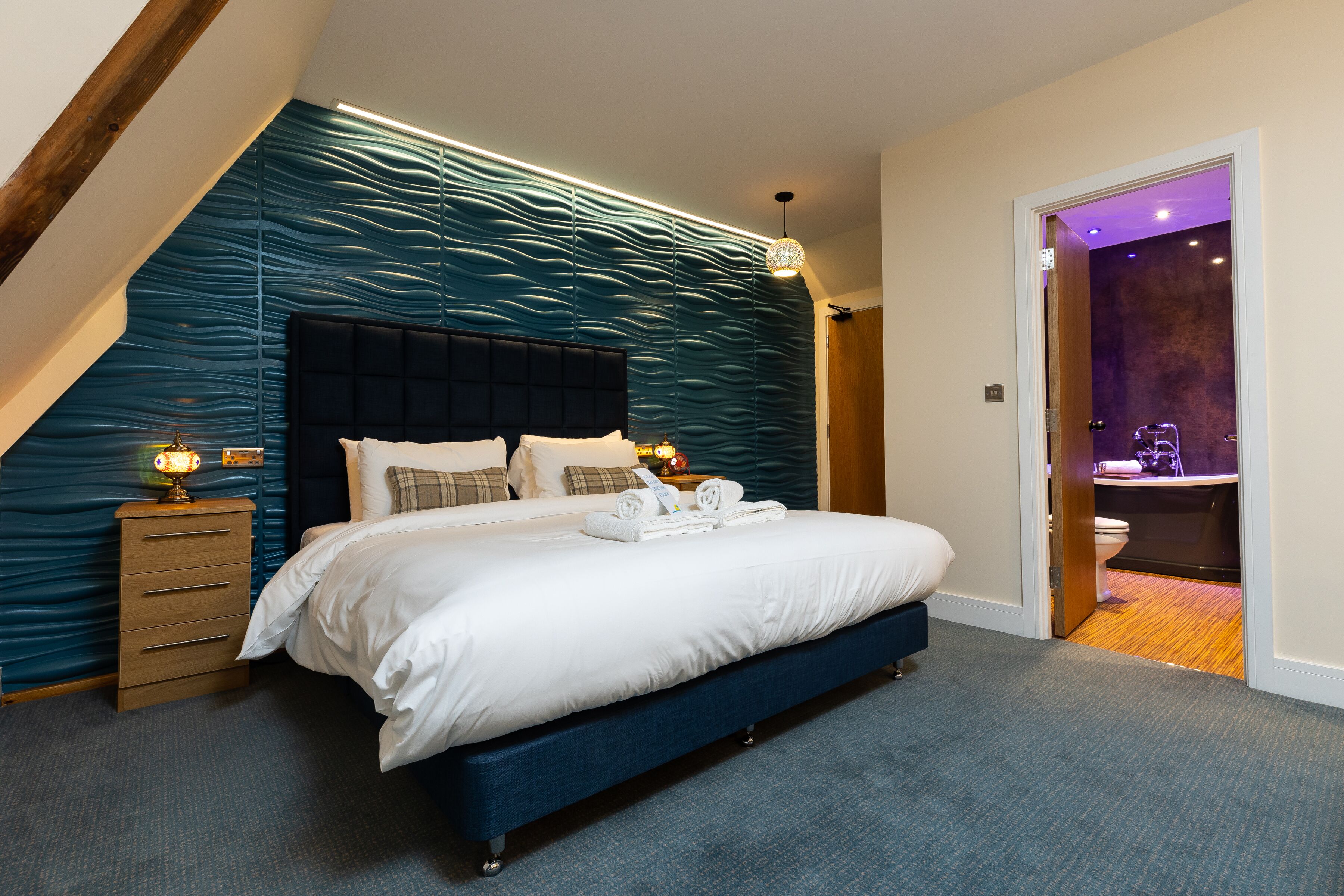 A modern bedroom with a large bed, a wooden nightstand, and a unique textured wall.