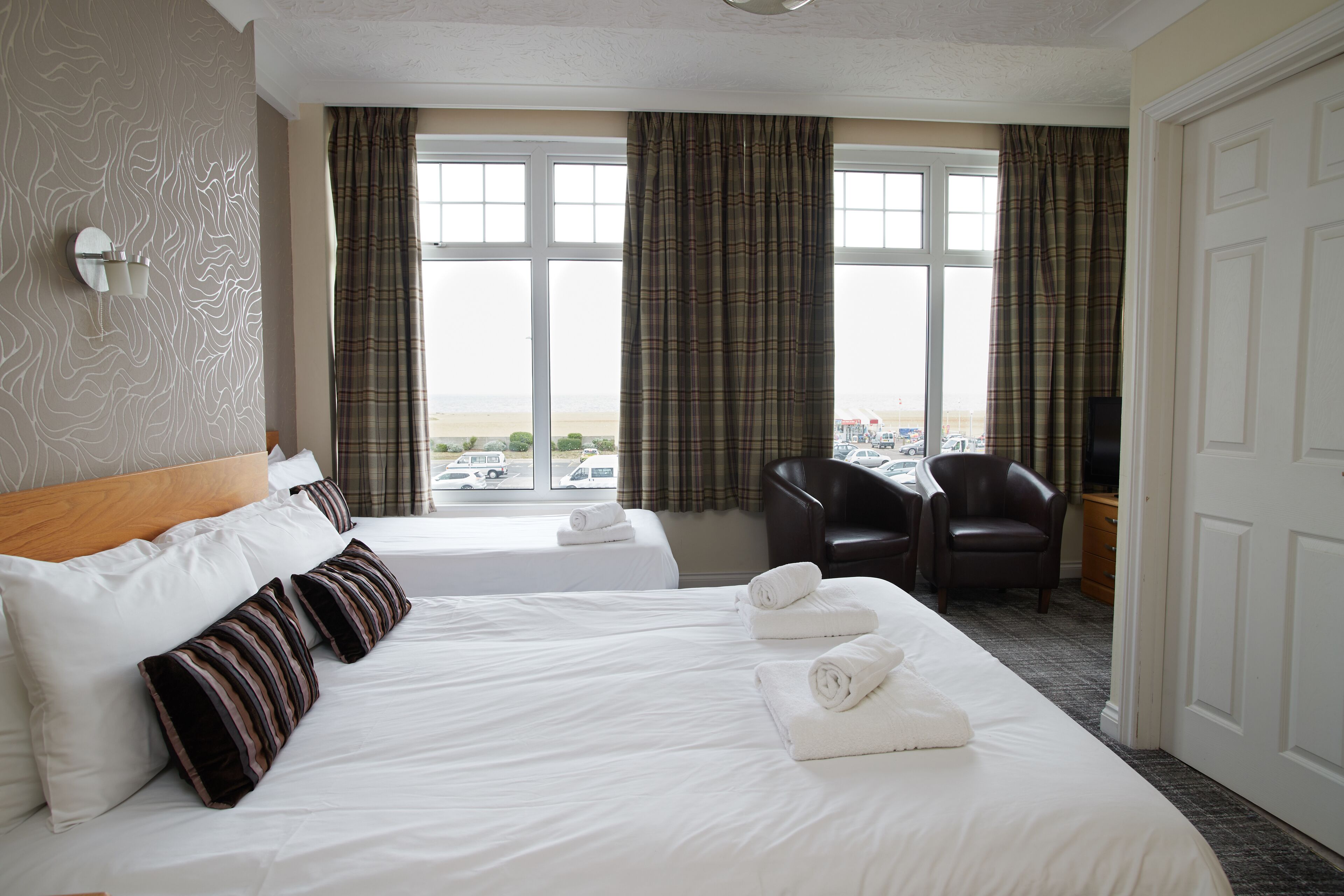 A hotel room with two beds, a view of the beach, a chair, and a television.