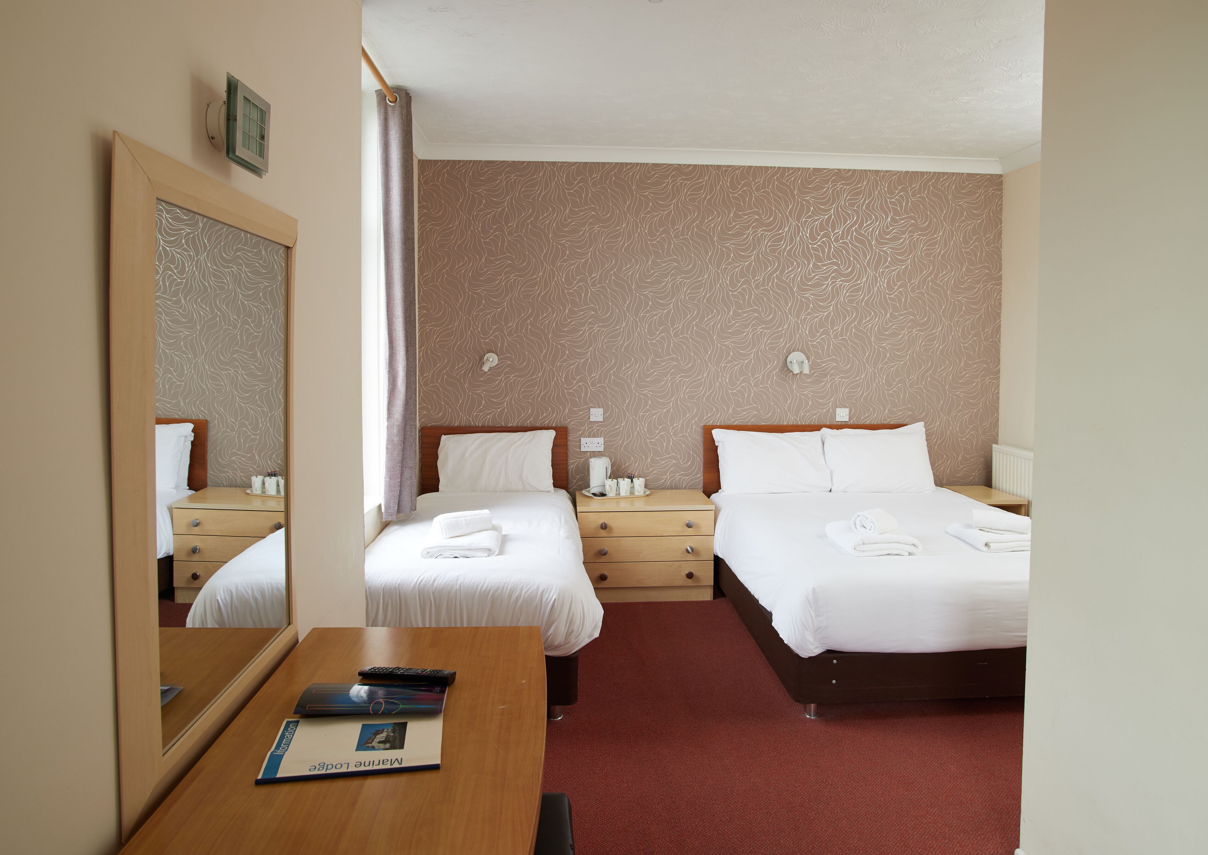 A hotel room with two beds, a wooden desk, a mirror, and a red carpet.