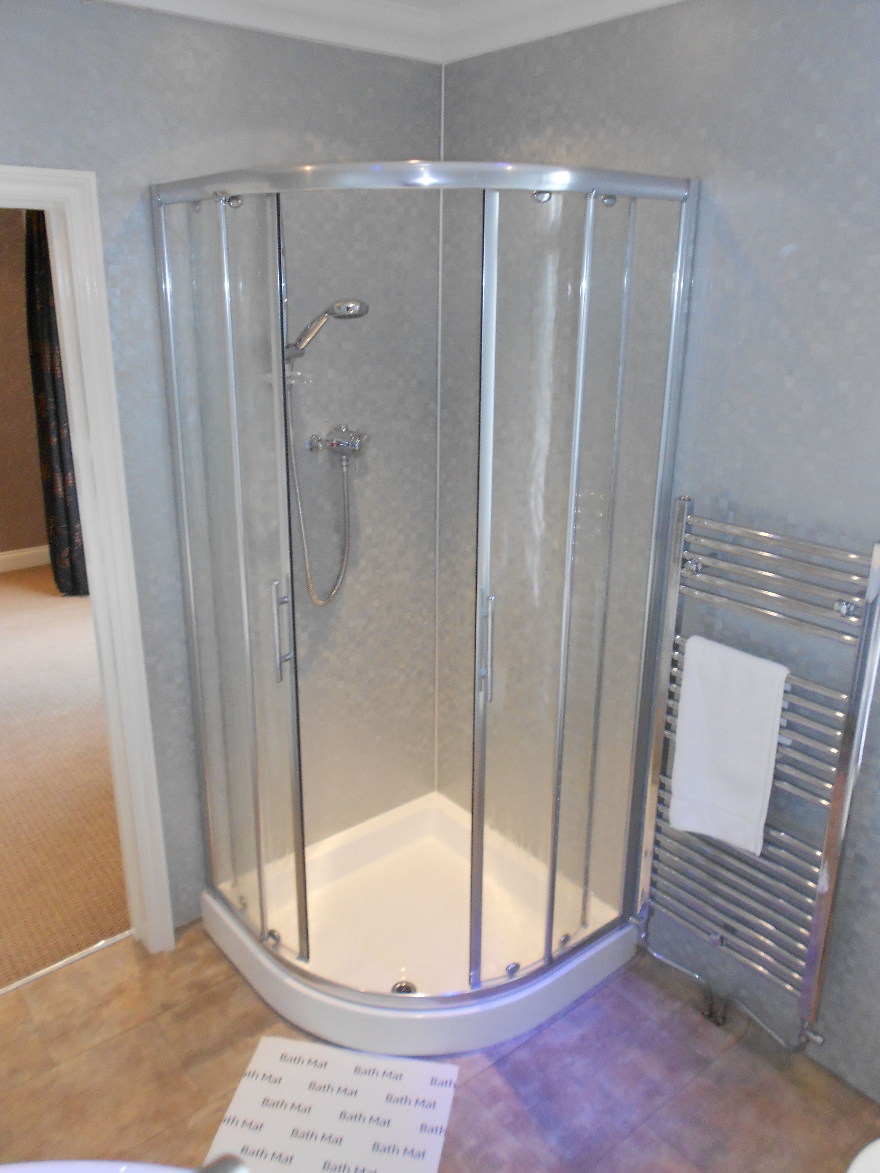 A glass-enclosed shower with a white floor, a towel rack, and a bath mat sign on the floor.