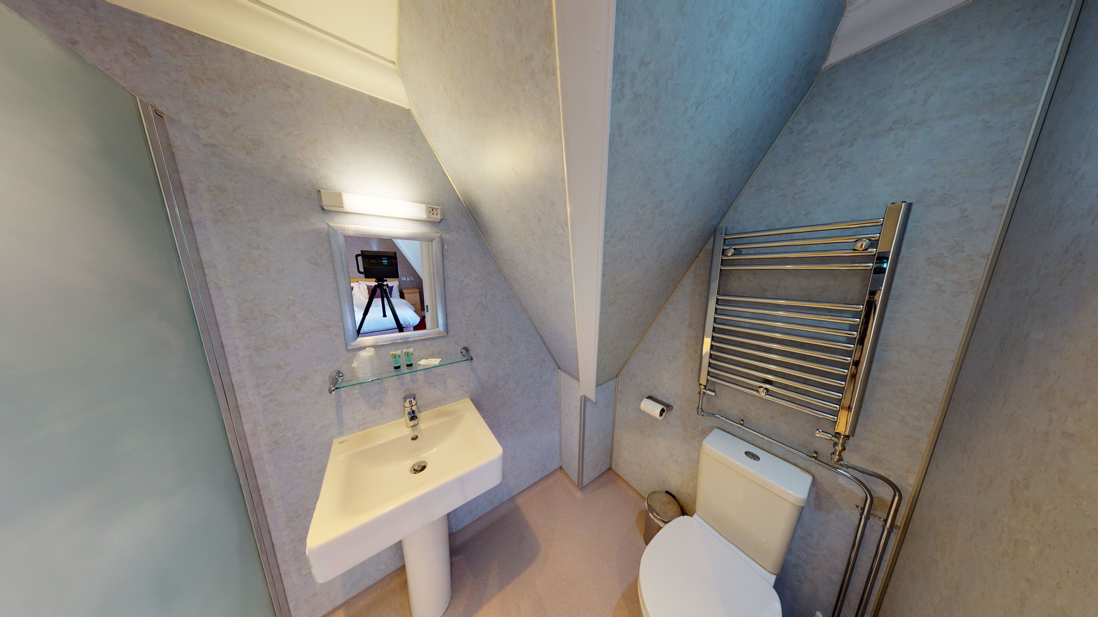 A modern bathroom with a pedestal sink, a toilet, a towel rack, and a mirror with a tripod.