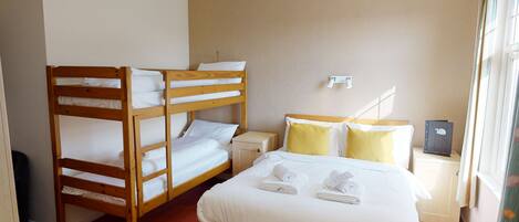 A hotel room with two wooden bunk beds, a single bed with white bedding, and a small bedside table with a lamp.