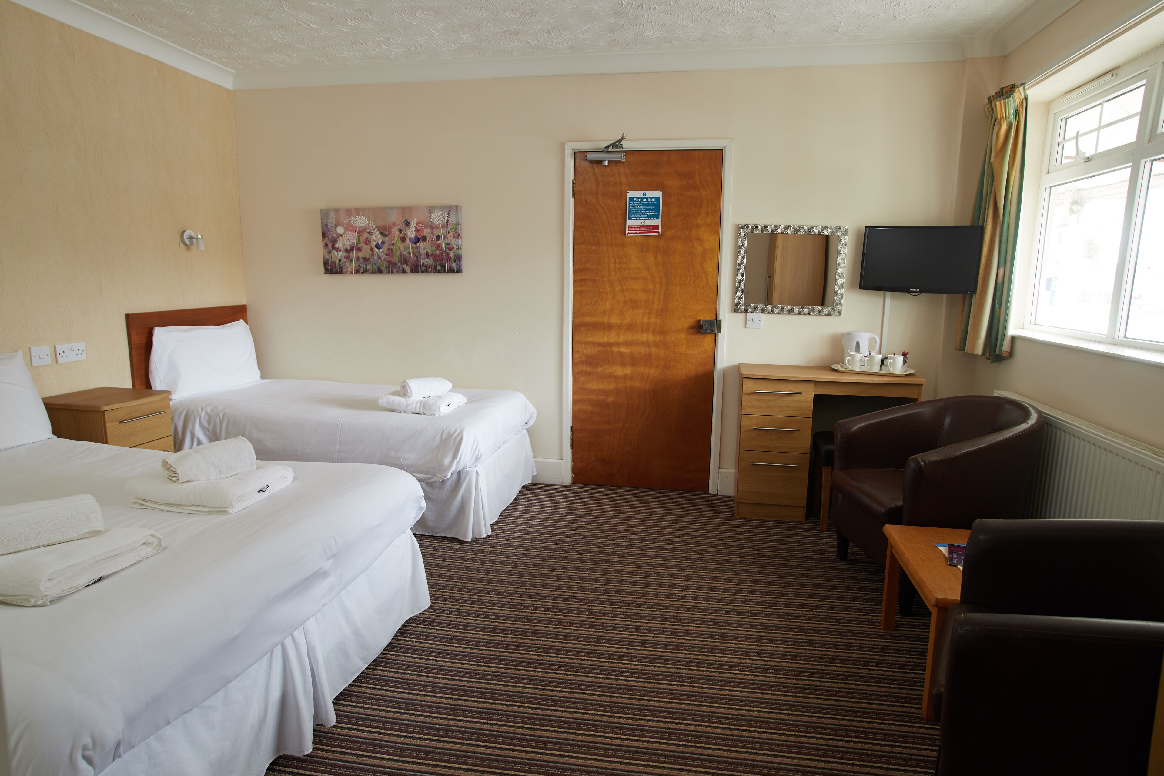 A hotel room with two beds, a desk with a chair, a television, and a door with a sign.