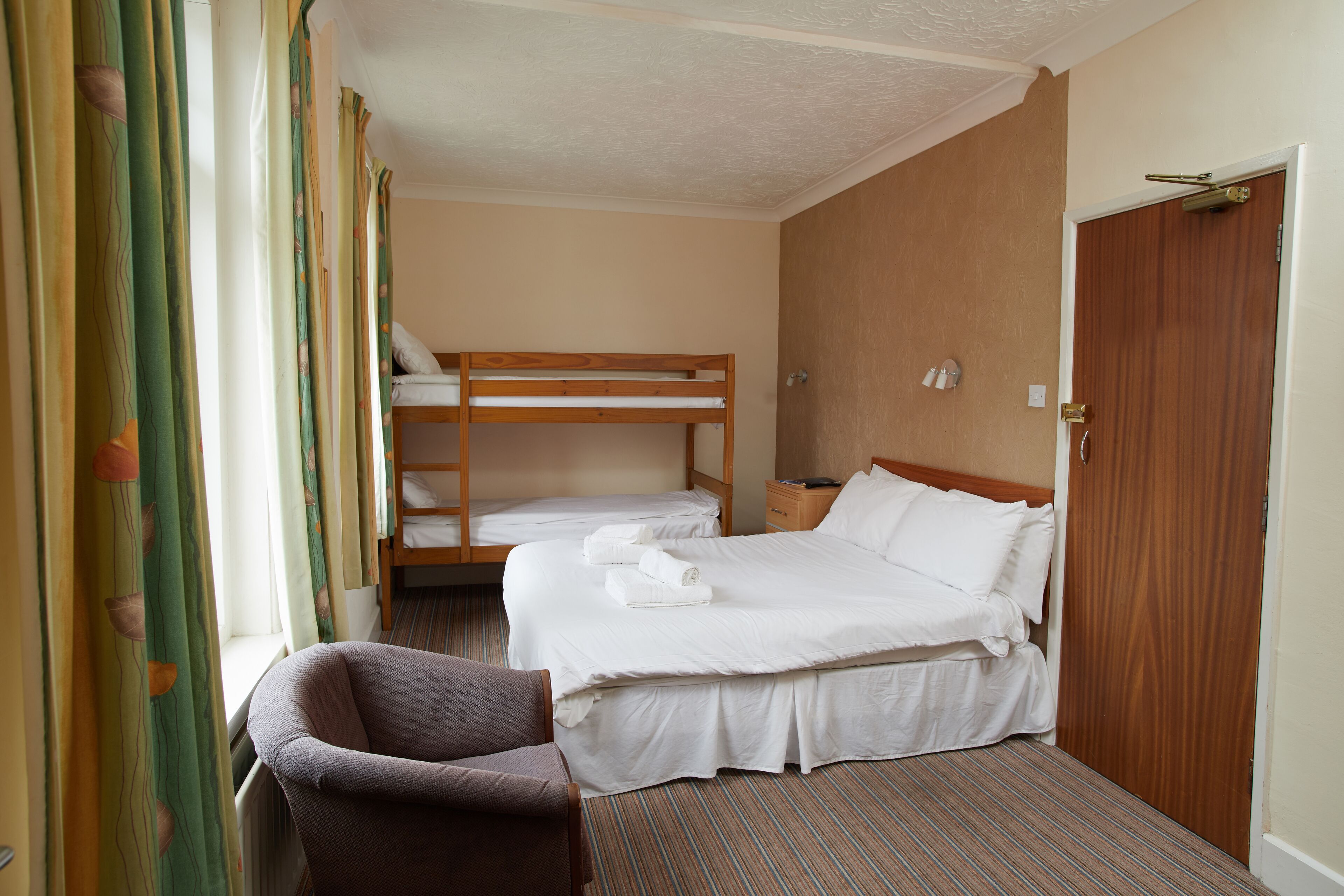 Une chambre d’hôtel avec un lit simple, une chaise et un lit superposé.
