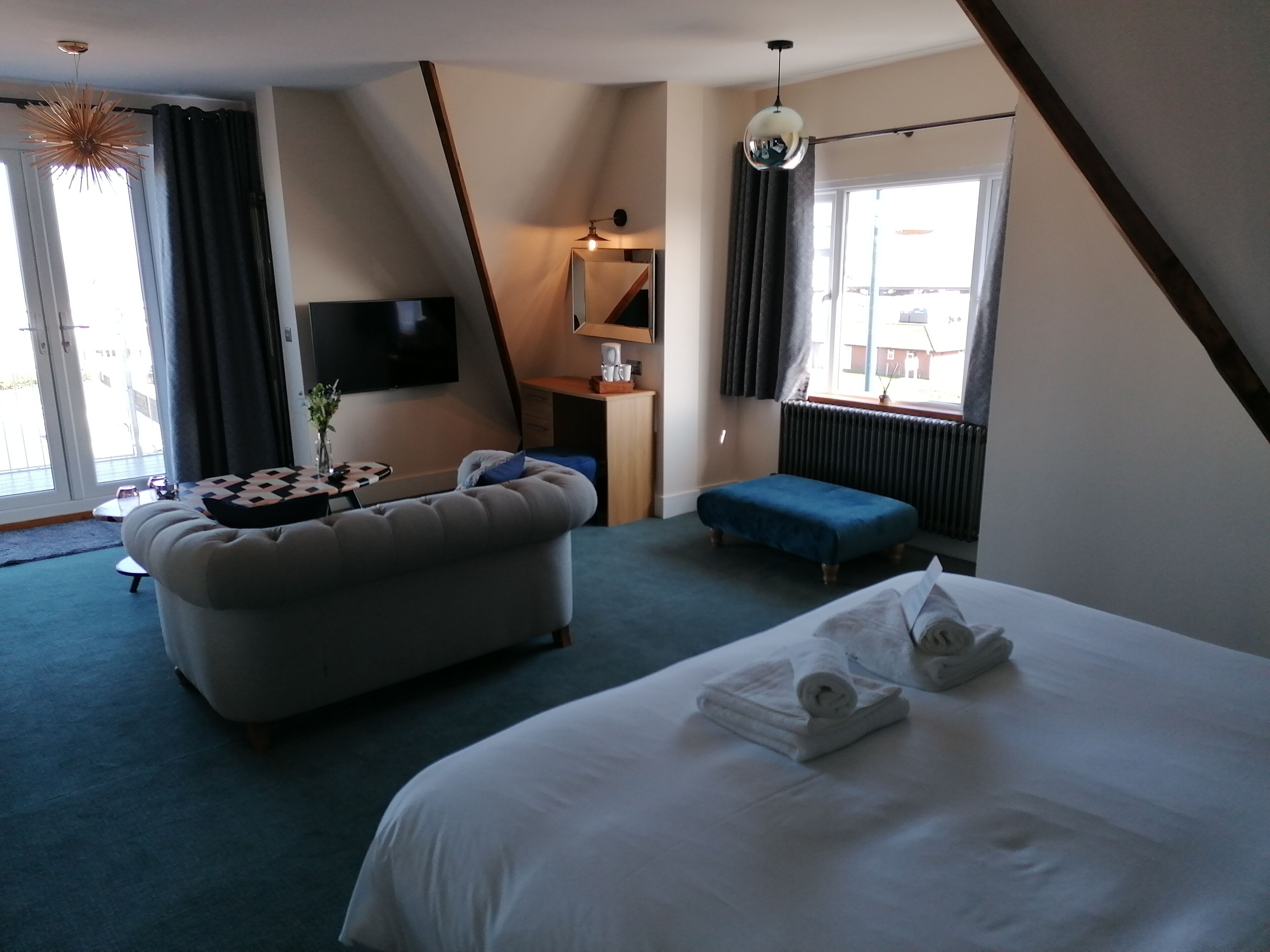 A hotel room with a large bed, a sofa, a small table, a TV, and a window with curtains.