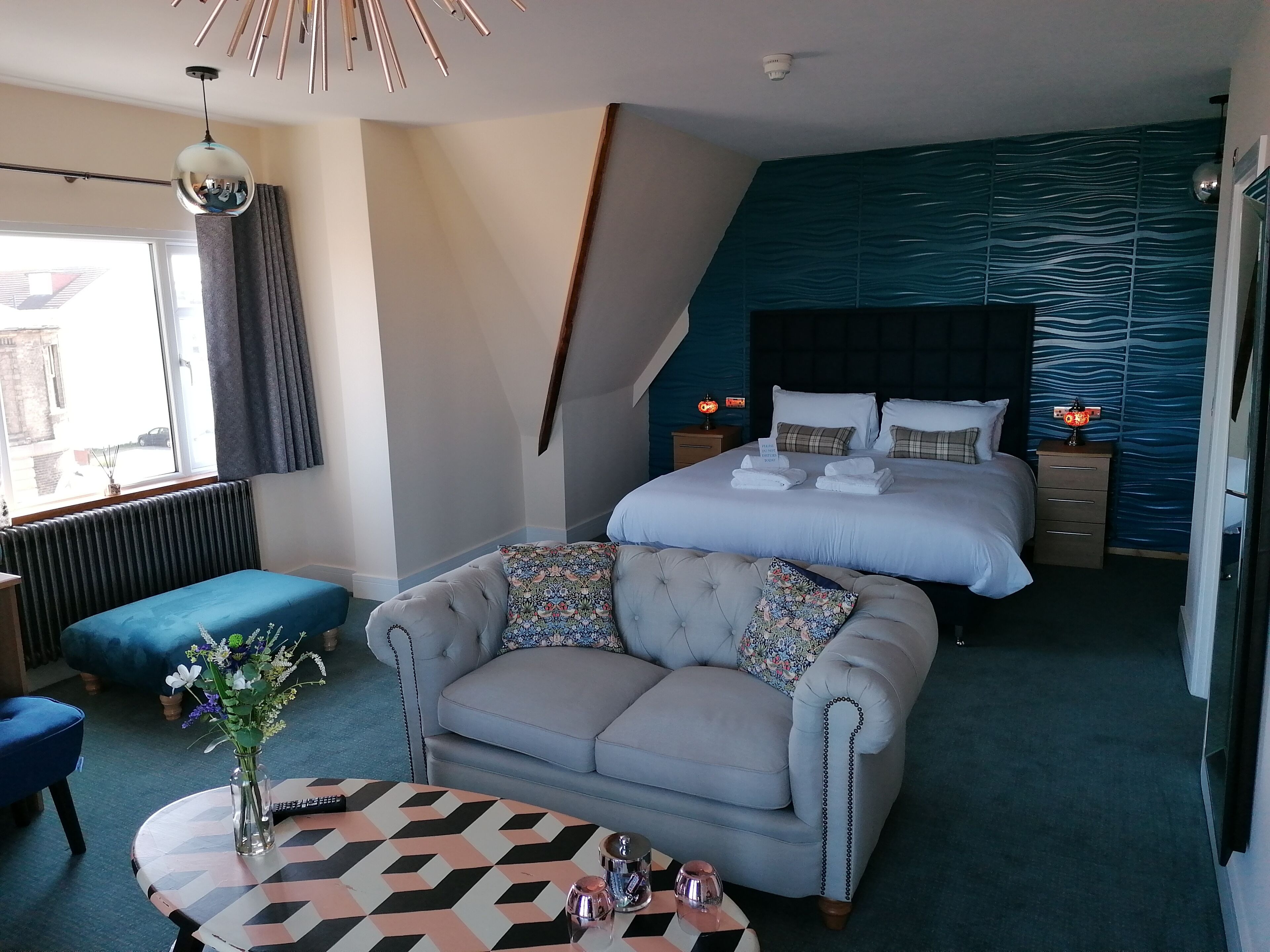 Ein modernes Hotelzimmer mit einem großen Bett, einer Couch, einem kleinen Tisch und Blick ins Freie.