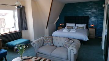 Ein modernes Hotelzimmer mit einem großen Bett, einer Couch, einem kleinen Tisch und Blick ins Freie.