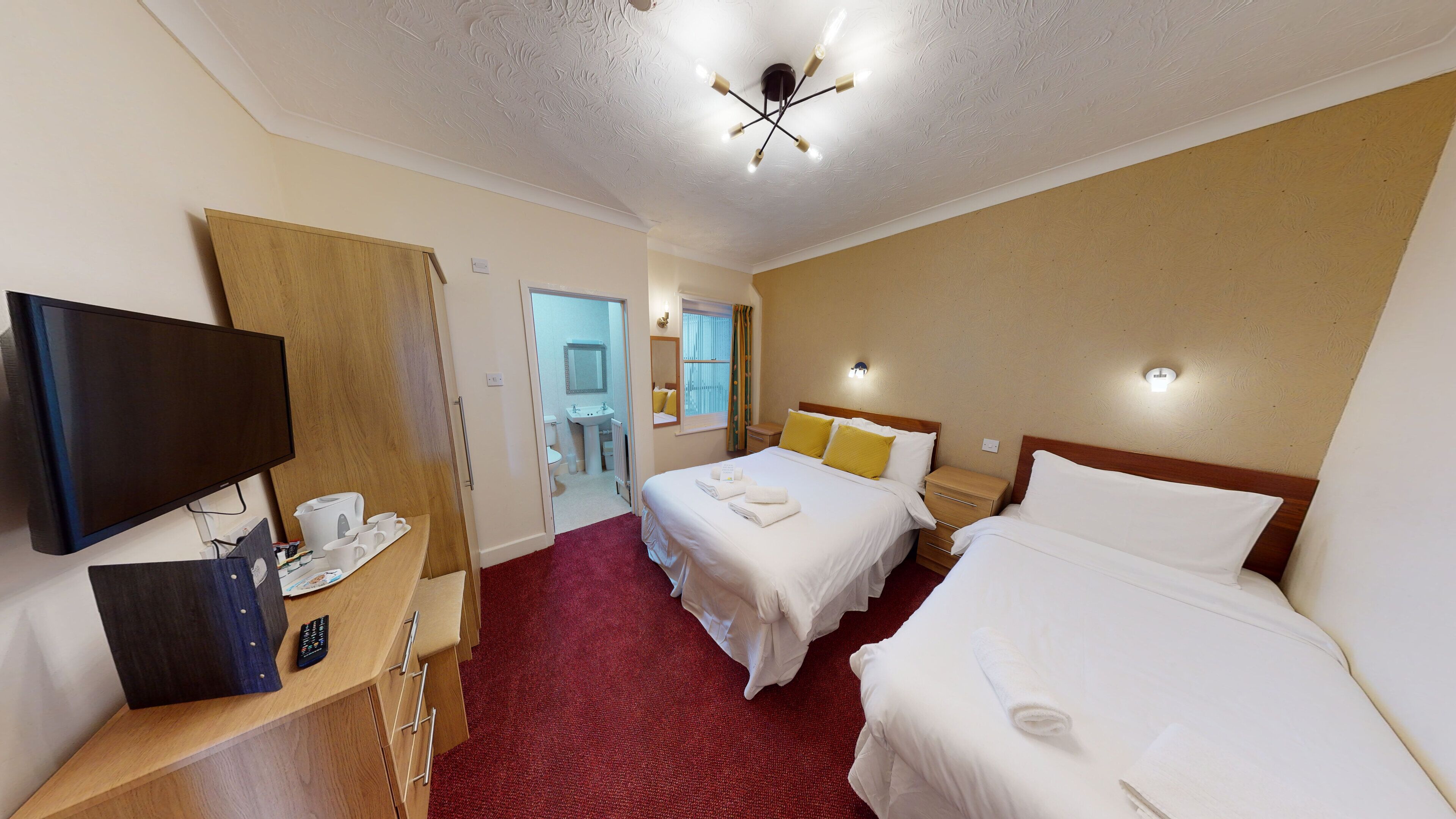 A hotel room with a TV, a desk with a coffee maker, two beds, and a bathroom visible through an open door.