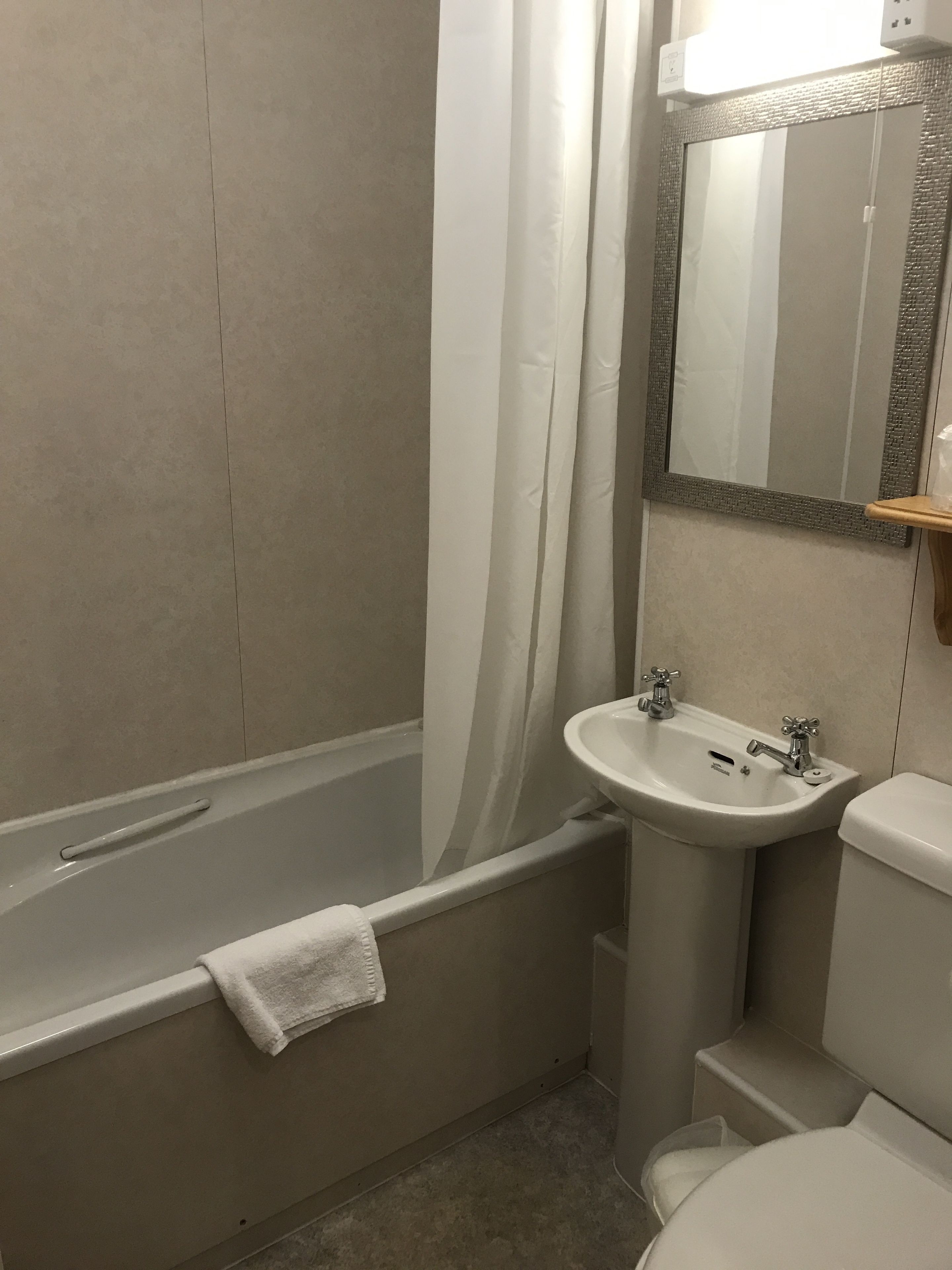 A bathroom with a bathtub, sink, toilet, and a mirror with a textured frame.