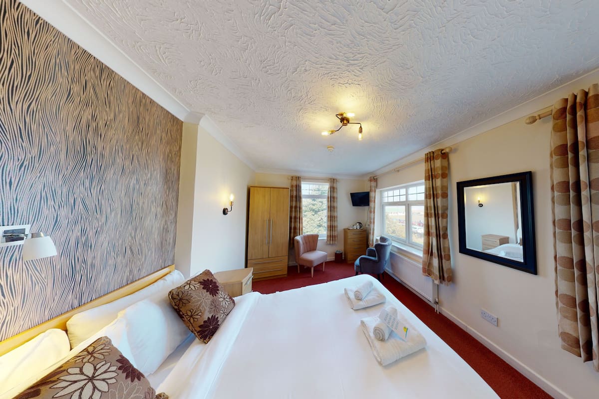 Een hotelkamer met een groot bed, een kledingkast, een bureau met stoel, een televisie en een raam met gordijnen.