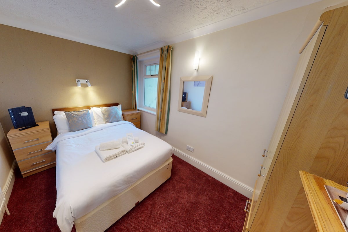 Een keurig ingerichte hotelkamer met een bed, nachtkastje en een spiegel aan de muur.