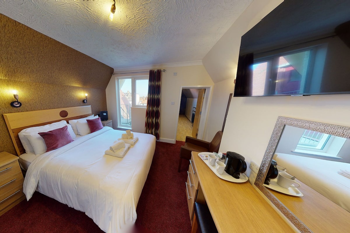 Een hotelkamer met een bed, een bureau met spiegel, een televisie en een raam met gordijnen.