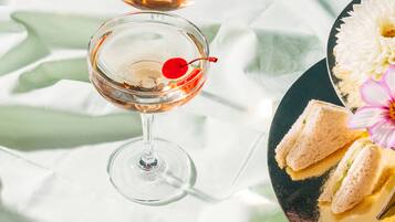 A table with two martini glasses, each with a cherry, and a plate with sandwiches and flowers.
