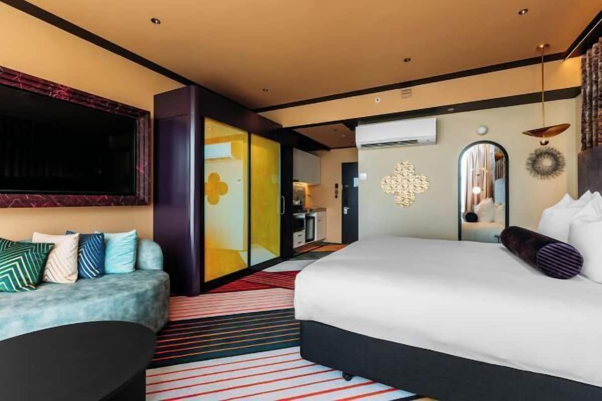 A modern hotel room with a large bed, a sofa, a TV, and a mirror.