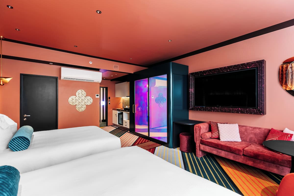 A hotel room with a large bed, a red sofa, a small table, and a TV.