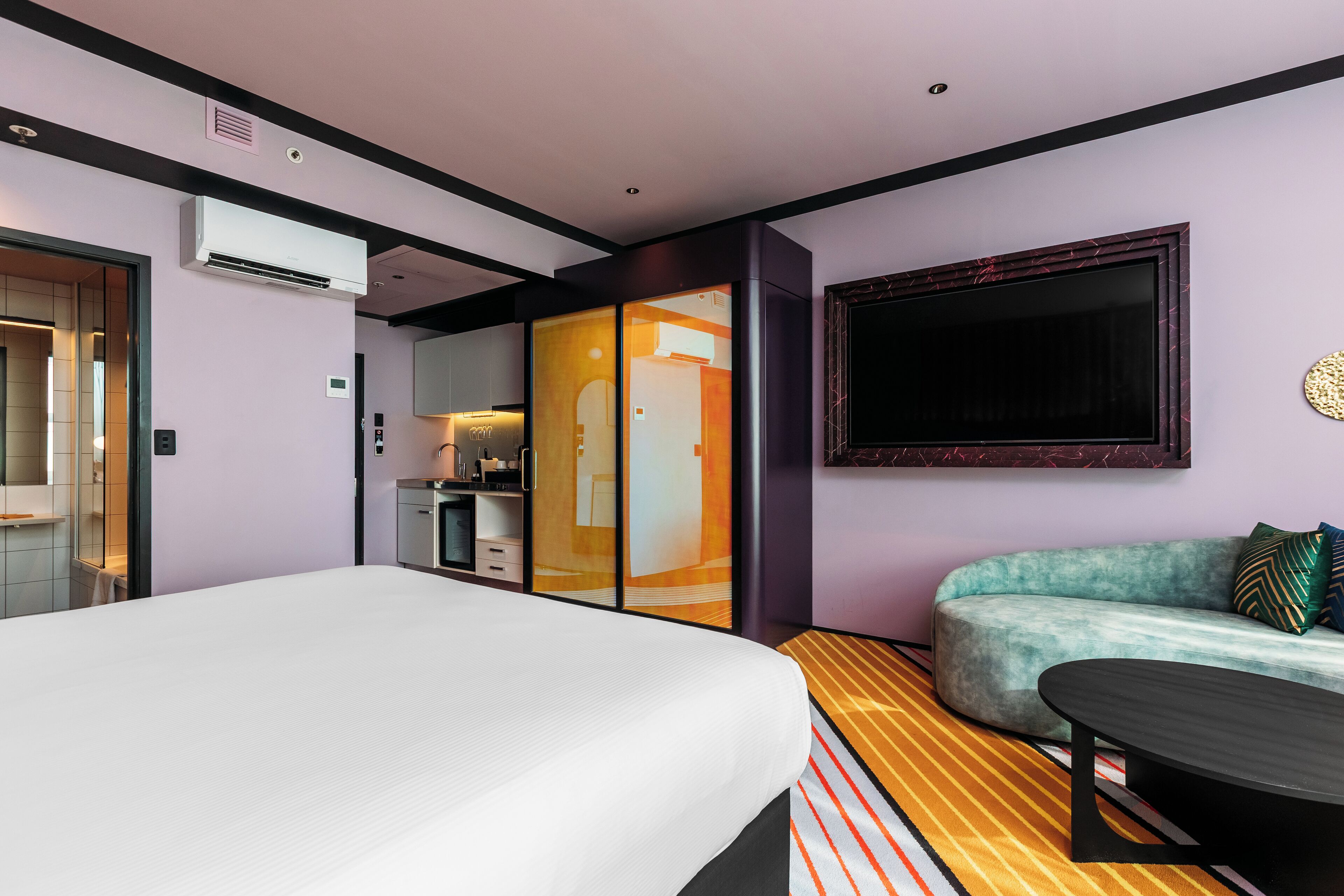 A modern hotel room with a large bed, a sofa, a TV, and a small table.
