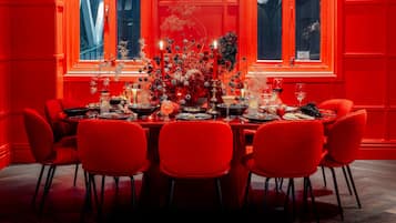 Mesa de comedor preparada para seis personas, con sillas rojas, velas y un centro de mesa floral.