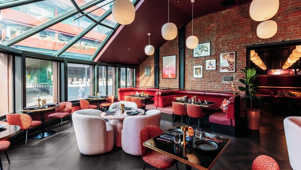 Un restaurant moderne avec de hauts plafonds, des murs en briques apparentes et de grandes fenêtres.