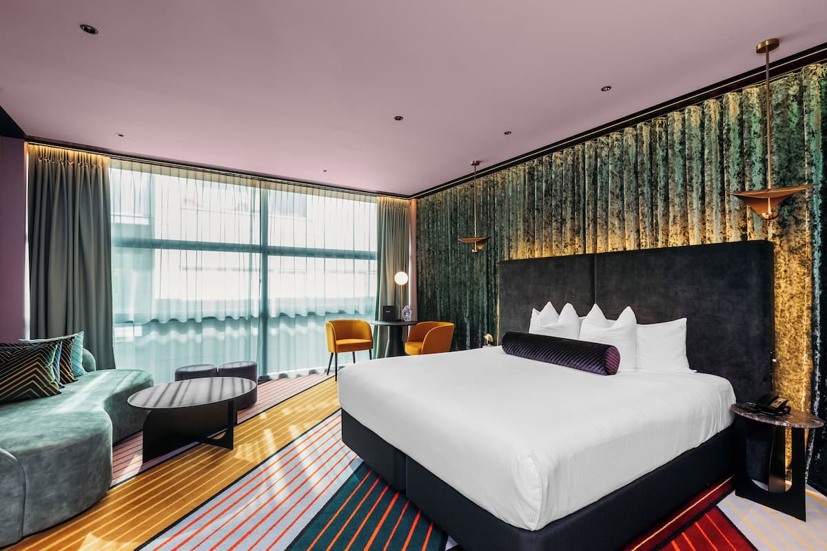 A modern hotel room with a large bed, a sofa, a small table, and a chair.